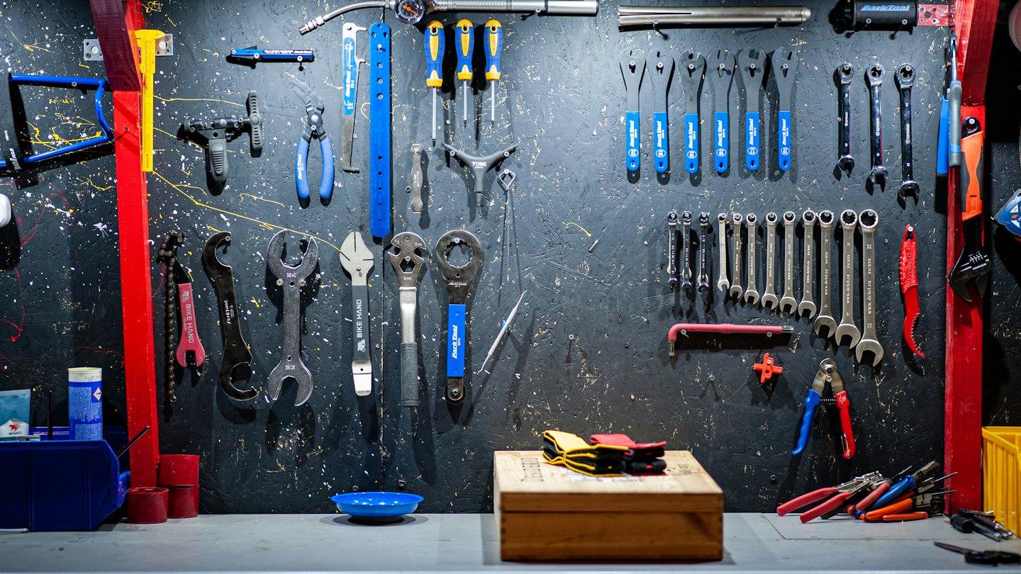 Various bicycle repair tools neatly hung on a workshop pegboard wall.
