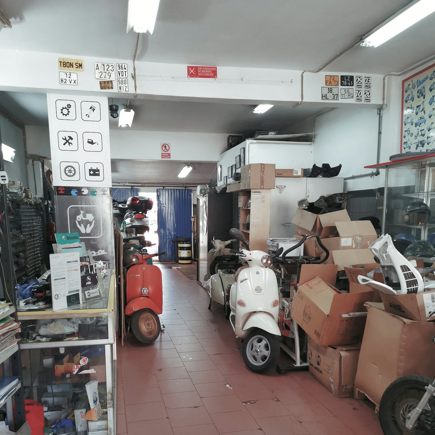 Classic scooters parked in a cluttered workshop with shelves of parts.